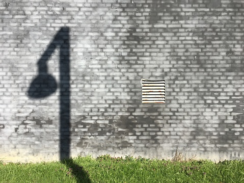 Street lamp casts its shadow on a weathered wall.