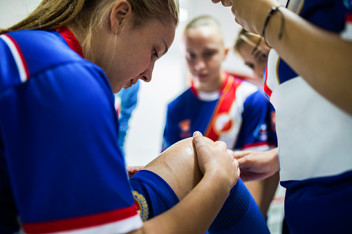 Teenage female soccer player holding her knee in pain at dressing room.