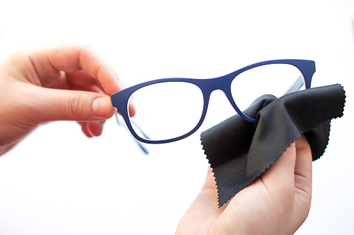 female hands are wiping spectacles with a microfiber fabric