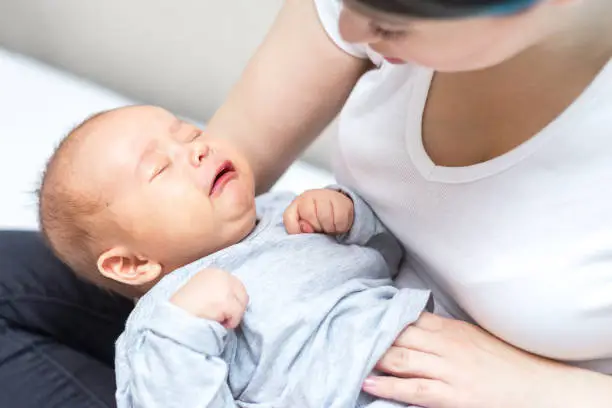 newborn is crying because of colic pain and his mother is soothing him