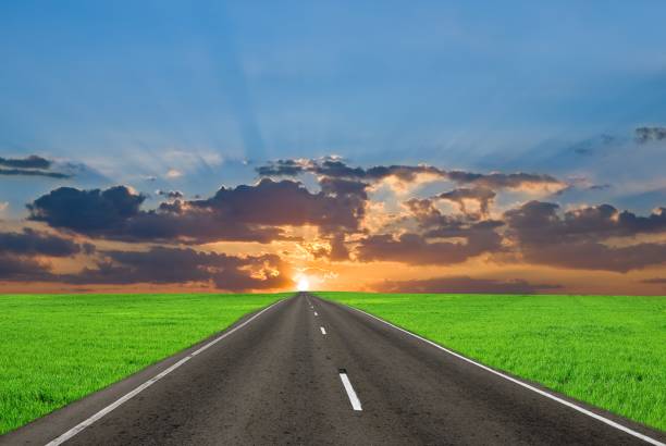 asphalt road among a green fields at the sunset