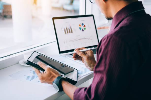istock Investors man holding pen pointing tablet to analyzing graphs on computer laptop in office. 1141371686