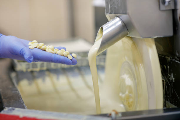 Holding white chocolate chips next to machine faucet Holding white chocolate chips next to melting machine faucet pouring chocolate sauce chocolate white chocolate chocolate chip white stock pictures, royalty-free photos & images