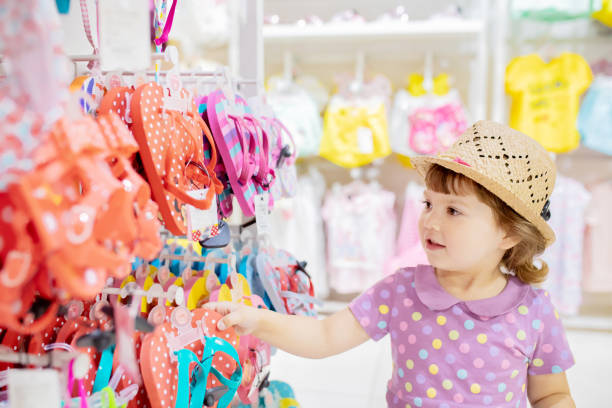 Cute little girl choosing clothes in the shop Adorable toddler girl in baby apparel store, buying slippers for summer. baby boutique stock pictures, royalty-free photos & images