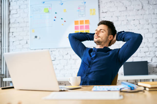 Businessman relaxing at work with hands behind head, eyes closed and coffee