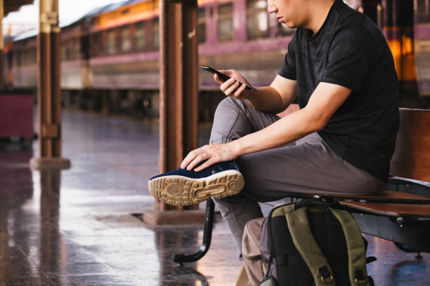 istock Young male tourist and backpacker using a phone while waiting for a public transportation inside train platform. 1141379312