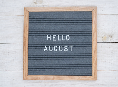 English text Hello August on a letter Board in white letters on a gray background. letter Board on white wooden background