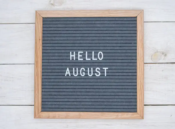 Photo of English text Hello August on a letter Board in white letters on a gray background