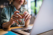 Close up of woman using a computer while holding a glass of water.