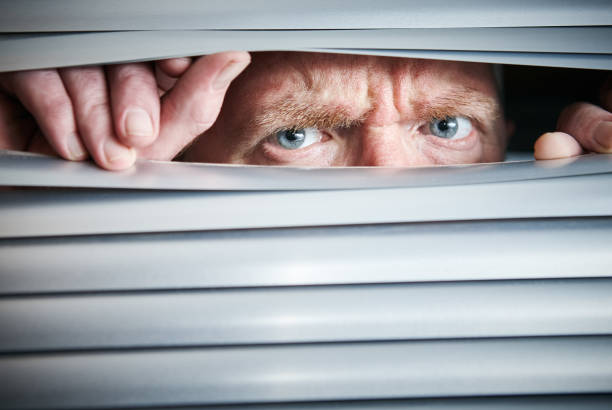 istock Man peers through closed blinds, looking worried 1141390298