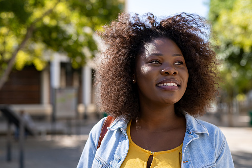 Portrait of curvy african woman thinking while looking away on the street. Closeup face of beautiful young african american woman smiling. Cheerful casual student girl with curly hair enjoying summer.