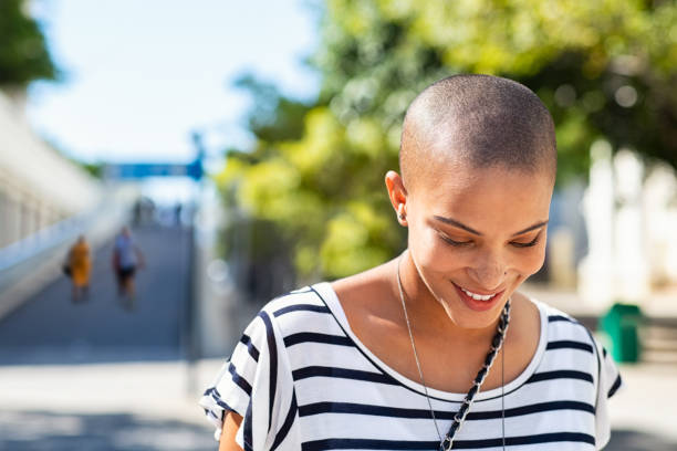 Young carefree woman smiling Portrait of happy and young bald woman smiling. Carefree trendy girl with bald head after cancer chemotherapy treatment. Stylish and beautiful woman feeling free in a city street. personal living stock pictures, royalty-free photos & images