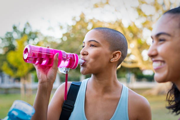 mujer deportiva bebiendo agua después del ejercicio - outdoors drinking women friendship fotografías e imágenes de stock