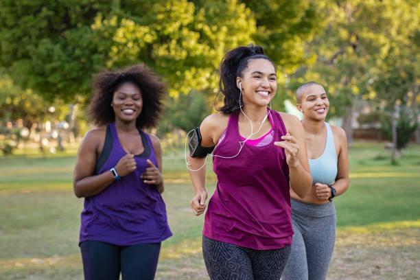 Active curvy women jogging Group of curvy girls friends jogging together at park. Beautiful smiling young women running at the park on a sunny day. Female runners listening to music while jogging. only women stock pictures, royalty-free photos & images