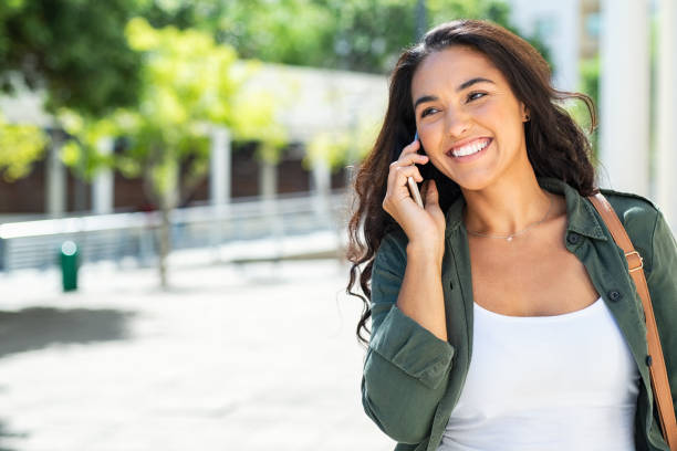 woman walking and talking on phone - spring happiness women latin american and hispanic ethnicity imagens e fotografias de stock