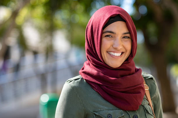 Muslim young woman wearing hijab Portrait of young muslim woman wearing hijab head scarf in city while looking at camera. Closeup face of cheerful woman covered with headscarf smiling outdoor. Casual islamic girl at park. arab culture photos stock pictures, royalty-free photos & images