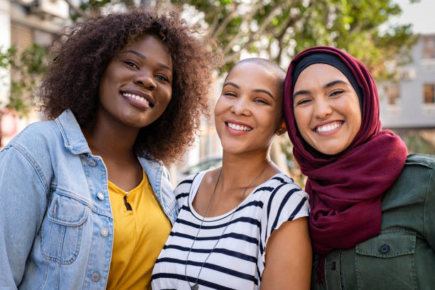 Multiethnic young friends enjoying together Group of three happy multiethnic friends looking at camera. Portrait of young women of different cultures enjoying vacation together. Smiling islamic girl with two african american friends outdoor. person of color stock pictures, royalty-free photos & images