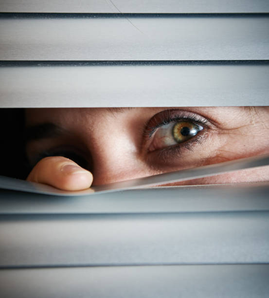 istock Suspicious woman peering through venetian blinds 1141394592