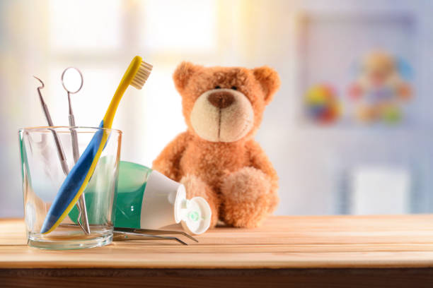 Dentist concept for children with tools in glass cup Dentist concept for children with tools in glass cup and teddy on wooden table in room with toys background. Horizontal composition. Front view pediatric dentistry stock pictures, royalty-free photos & images