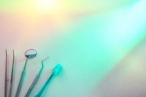 Dentist tools on white table illuminated with green light. Horizontal composition. Top view