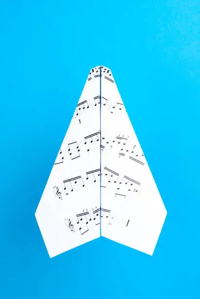 Photo of Paper jet /paper airplane made of a music score. Music score paper plane on blue