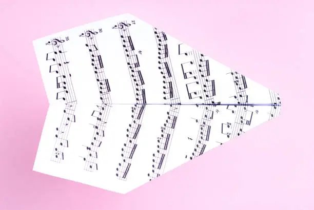Photo of Paper jet /paper airplane made of a music score. Music score paper plane on pink
