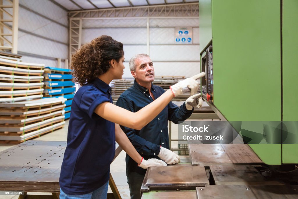Instructor discussing with trainee in factory Mature engineer and female trainee discussing over puller machine. Instructor is teaching apprentice in factory. They are in industry. Guidance Stock Photo