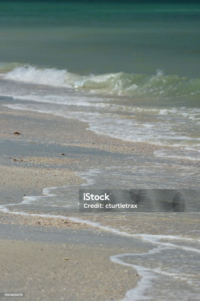 Turquoise sea with small waves breaking and washing up onto tan beach sand Bright sand with small surf and light-colored sea water with suspended sediment near the sore, leading to deep, dark water further out. Photo taken at Caladesi & Honeymoon Island state parks in Clearwater, Florida. Nikon D7200 with Nikon 200mm Macro lens Beach Stock Photo