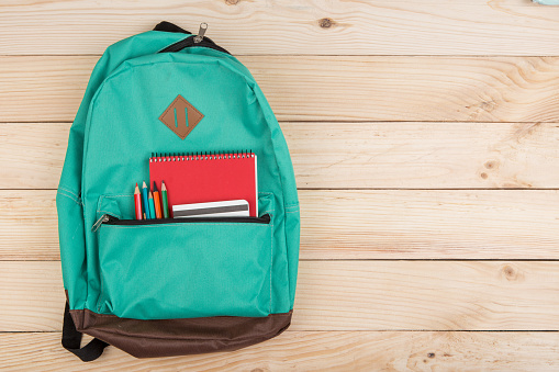 Education concept - blue backpack, red notebooks and pencils on wooden table