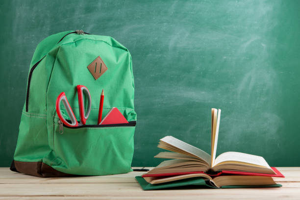 istock green backpack, red scissors and notebook and book on the background of the blackboard 1141404620