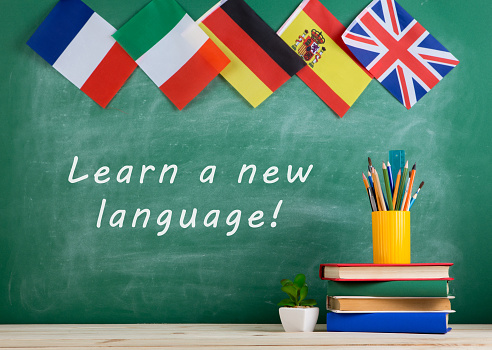 Learning languages concept - flags of Spain, France, Great Britain and other countries, blackboard with text 