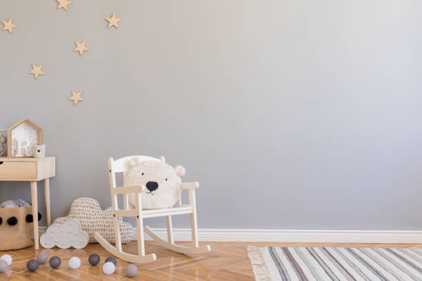 Stylish scandinavian newborn baby room with toys, children's chair, natural basket with teddy bear and small shelf. Modern interior with grey background walls, wooden parquet and stars pattern. Stylish and modern scandinavian newborn baby interior with mock up photo or poster frame on the white shelf. nursery bedroom stock pictures, royalty-free photos & images