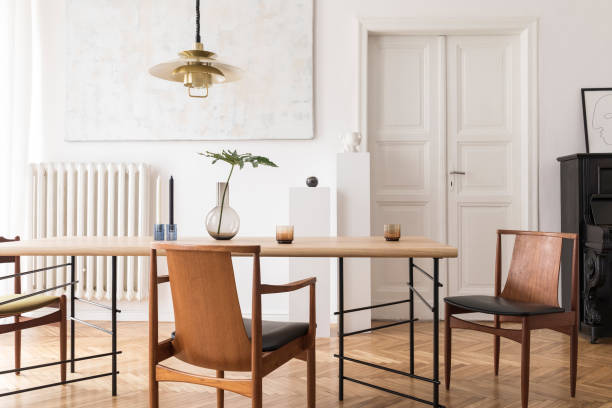istock Eclectic and elegant dining room interior with design sharing table, chairs, gold pendant lamp, abstract paintings, piano and stylish accessories. Minimalistic decor. Brown wooden parquet. Real photo. 1141409342