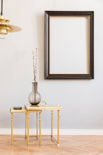 istock Stylish and design retro interior with design gold lamp and small table with vase. Black mock up frame on the grey background wall. Minimalistic concept of sitting room. Real photo. 1141409401