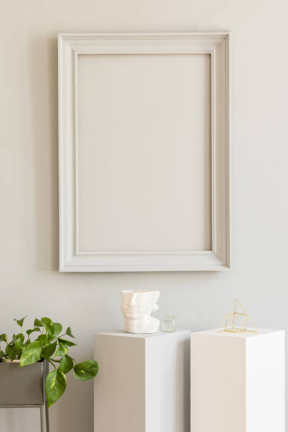 istock Minimalistic and design home decor with mock up grey poster frame and white pedestals with stylish accessories and platns. Eclectic and modern room interior. Template. Blank. Real photo. 1141409582