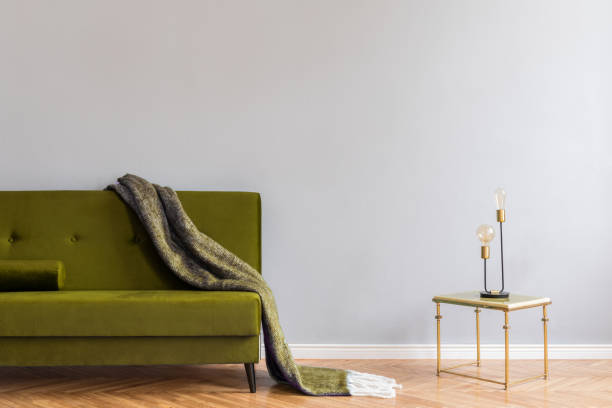 istock Minimalistic and luxury grey home interior with green velvet design sofa,blanket, gold coffe table with table lamp. Copy space for inscription, mock up poster. Empty wall. Brown wooden parquet. 1141410929