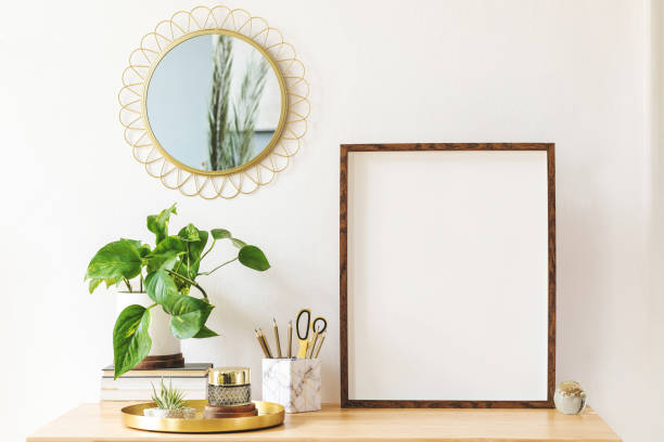istock Modern scanidnavian interior with mock up photo frame, design office accessories and plants on the wooden desk. Beautiful mirror on the white wall. Creative desk of home decor. Warm and sunny room. 1141410933
