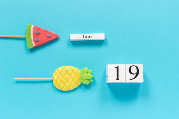 деревянные кубики календарной даты 19 июня и летние фрукты конфеты ананас, арбуз леденцы на палочке на синем фоне. концепция отпуск или праз� - june the nineteenth стоковые фото и изображения