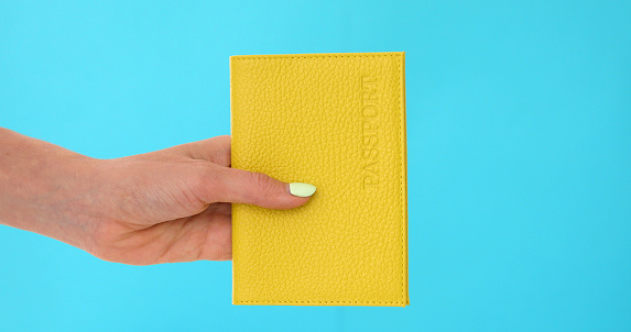 Woman's hand holding a red passport against blue background