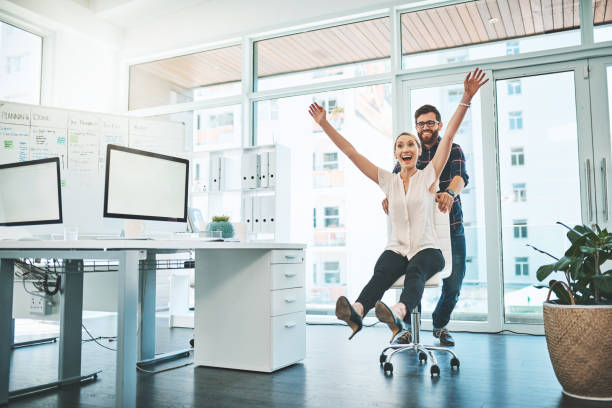 We believe in both working hard and having fun Shot of a businessman pushing his colleague around in a chair in an office arms raised women business full length stock pictures, royalty-free photos & images