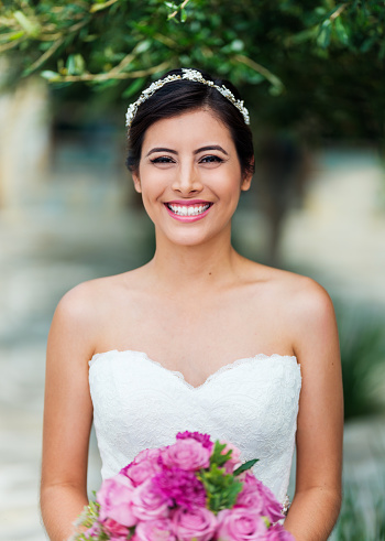 Portrait of a happy latin bride holding a bouquet of flowers and smiling at the camera.