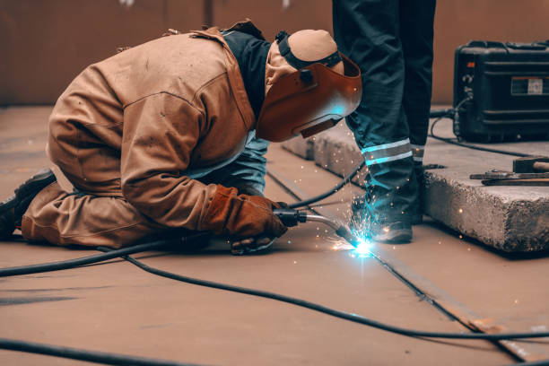 istock Worker in protective suit and mask crouching and welding in metal tower at construction site. 1141425048