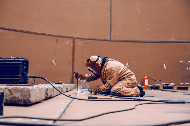 istock Worker in protective suit and mask crouching and welding in metal tower at construction site. 1141425200