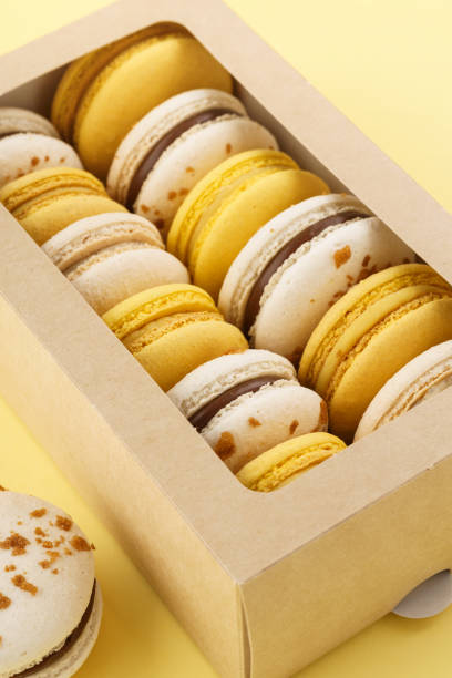 Colorful macarons in a gift box on yellow background.