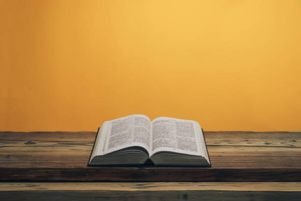 istock Open Holy Bible on a old oak wooden table. Orange wall background. 1141427207
