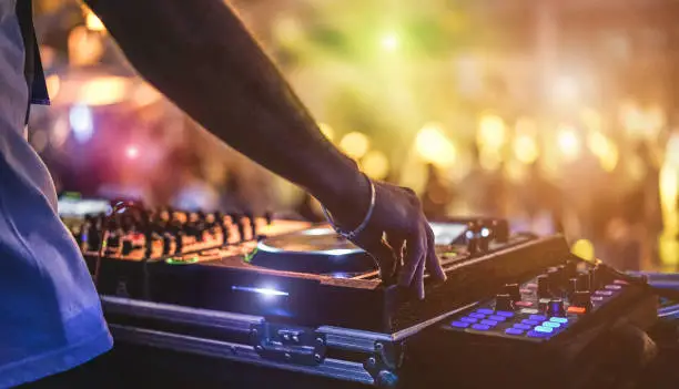 Photo of Dj mixing outdoor at beach party festival with crowd of people in background - Summer nightlife view of disco club outside - Soft focus on hand - Fun ,youth,entertainment and fest concept