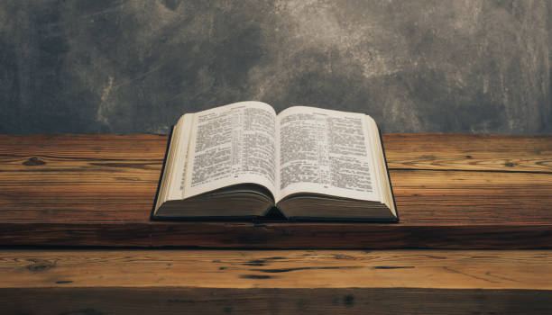 istock Open Holy Bible on a old oak wooden table.  Grey wall background. 1141428010