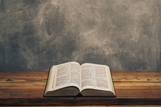 istock Open Holy Bible on a old oak wooden table.  Grey wall background. 1141428574