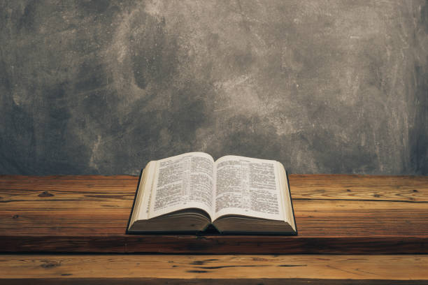 istock Open Holy Bible on a old oak wooden table.  Grey wall background. 1141428932