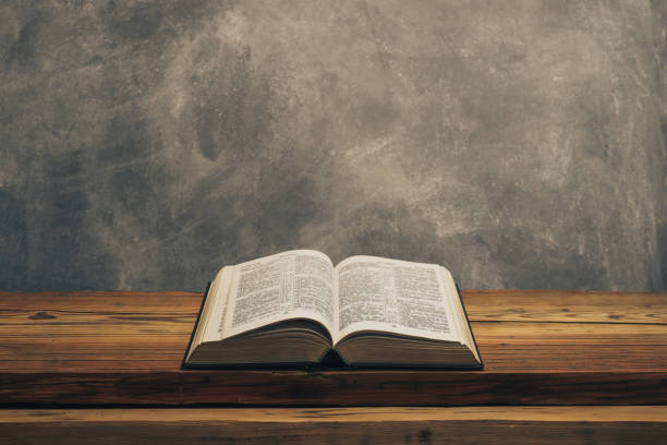 istock Open Holy Bible on a old oak wooden table.  Grey wall background. 1141428970